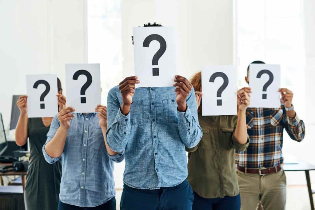 a group of people holding up paper with question marks